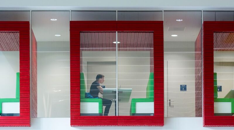Contemporary coworking space with colorful booths and glass walls featuring a focused professional. - Photo by Jan van der Wolf on Pexels